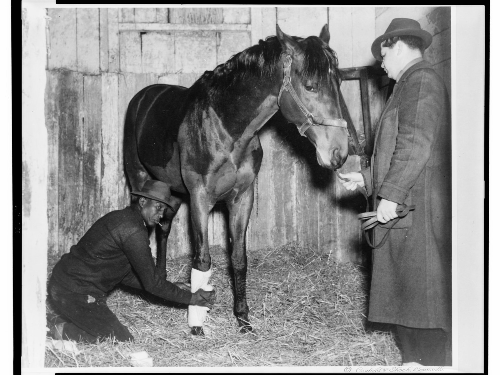 Representative 1940 archival scene of an African American man bandaging a horse's right foreleg while another man holds the rein; not documented as Lexington or the Kentucky Association Track, the exact occupations of the depicted men are not documented, and the image was made after the track closed
