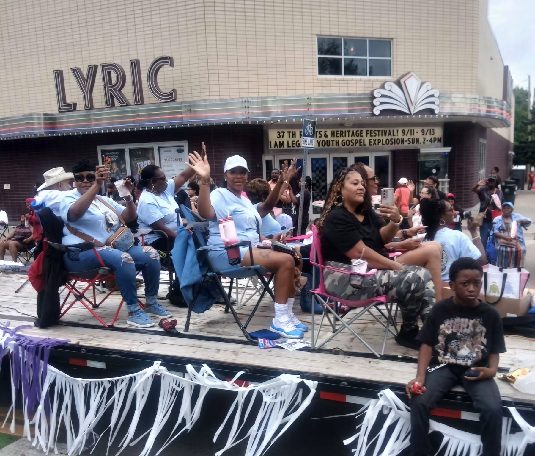 Festival attendees riding on a parade float and waving in front of the Historic Lyric Theatre