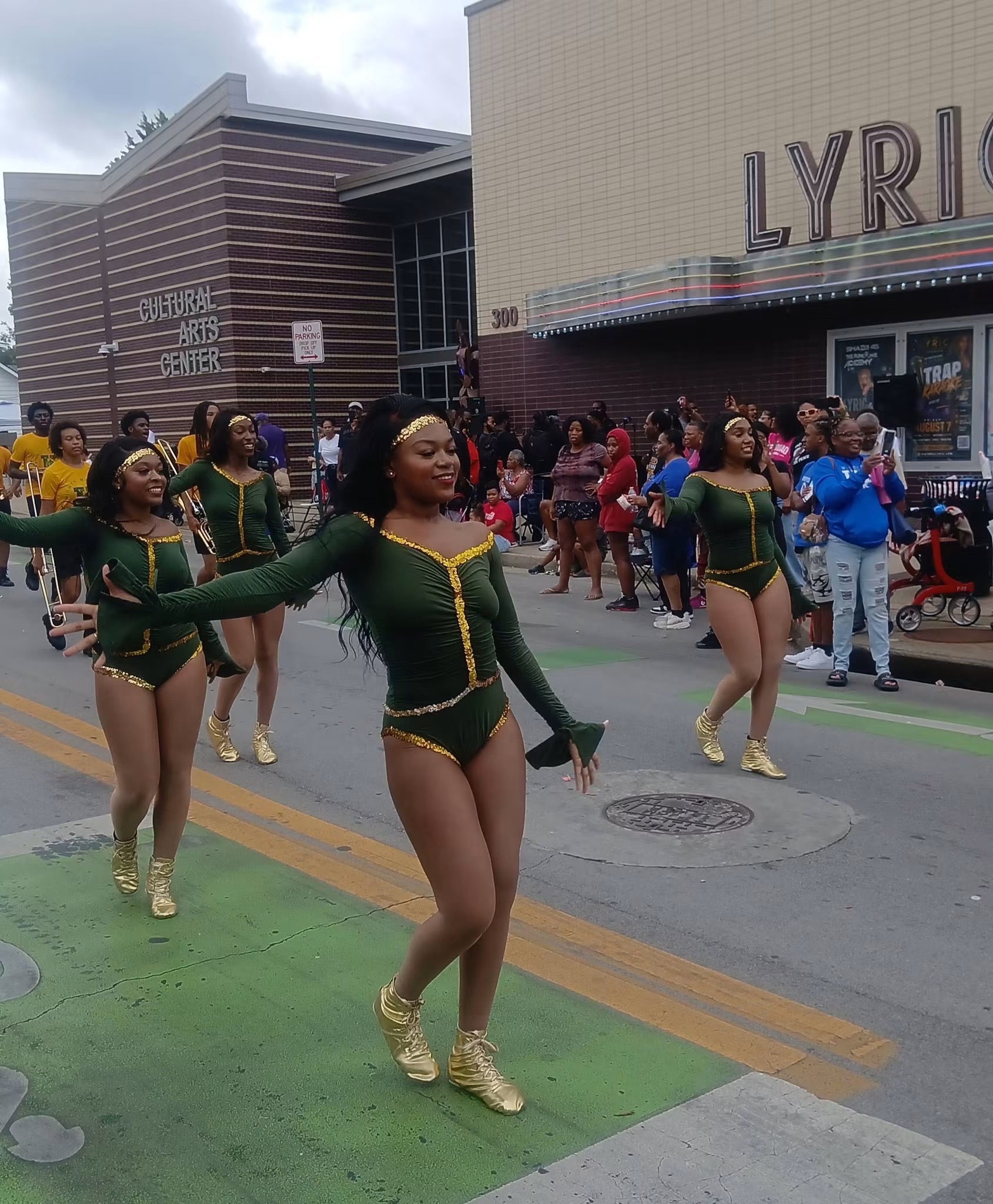 Dancers in green-and-gold costumes performing during the Roots and Heritage parade outside the Historic Lyric Theatre