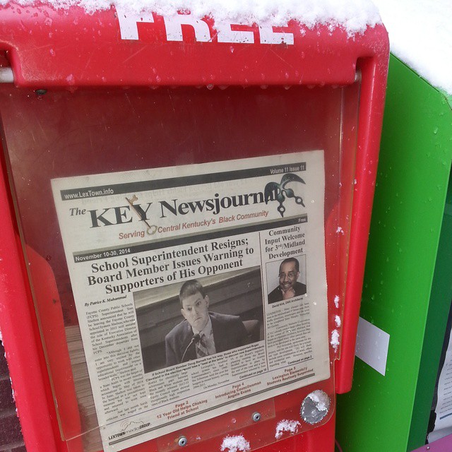 A red free newspaper box outside the Lyric Theatre displays the November 2014 Key Newsjournal, with snow on its lid.